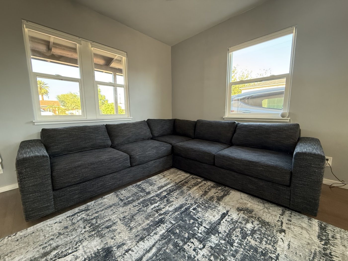 A gray sectional couch under two windows in a living room