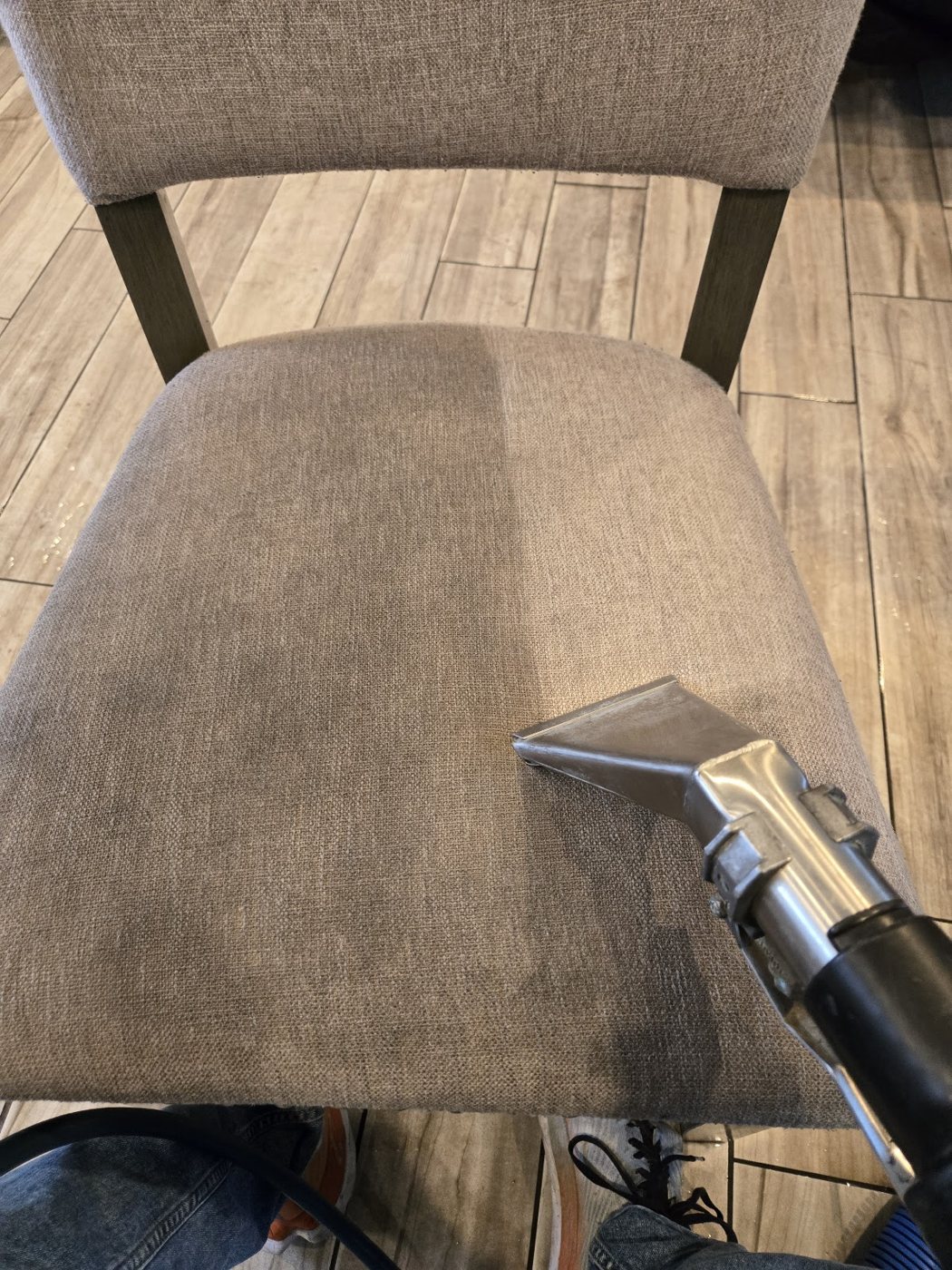 A cleaning tool lifting dirt from a gray upholstered chair seat